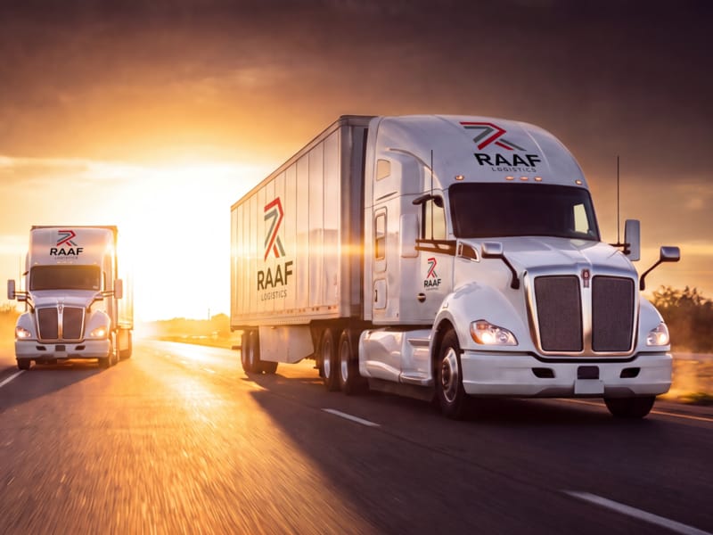 Two RAAF Logistics tractors with 53-foot dry vans on a highway at sunrise